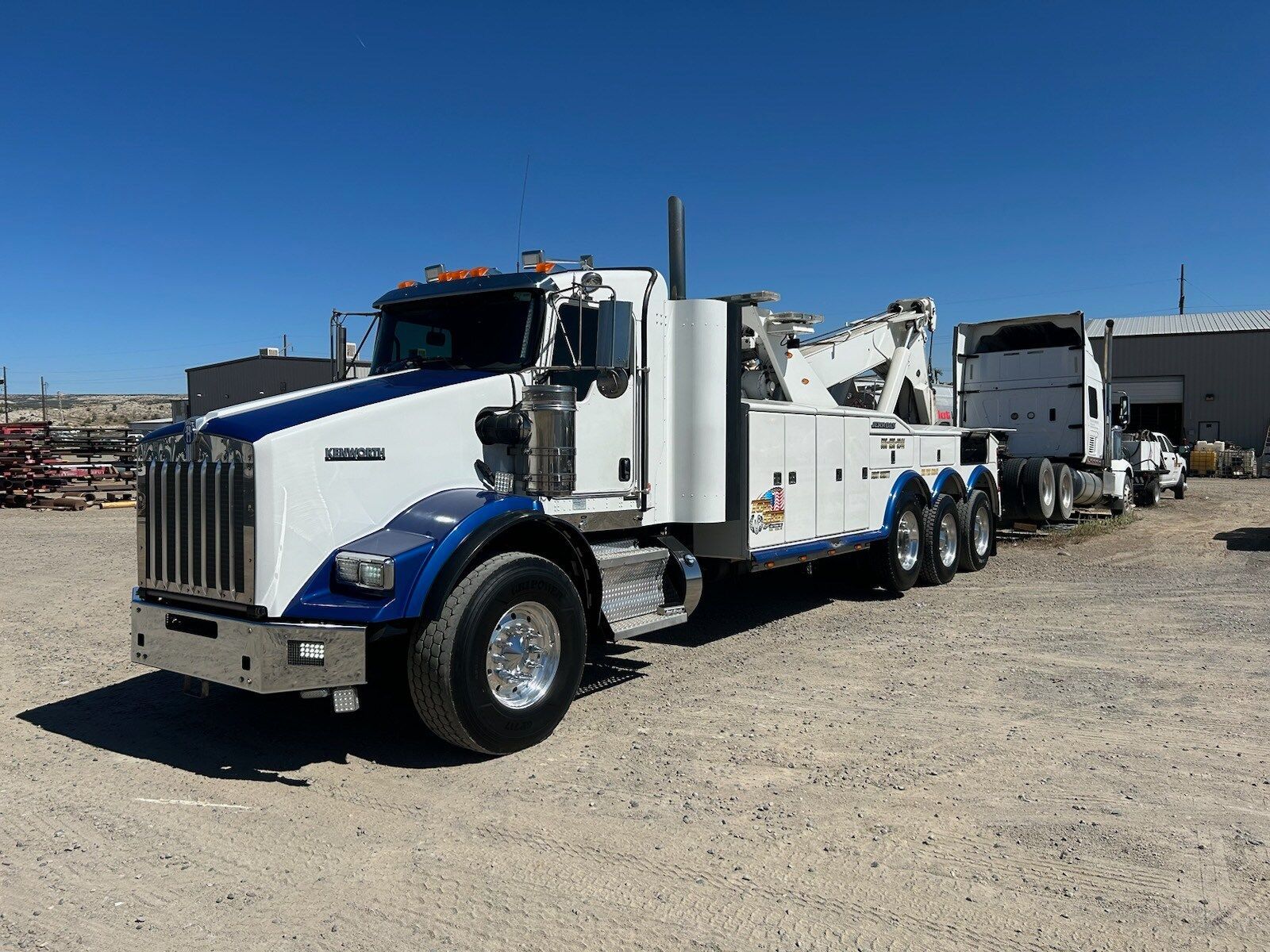 A white and blue tow truck is parked in a dirt lot.