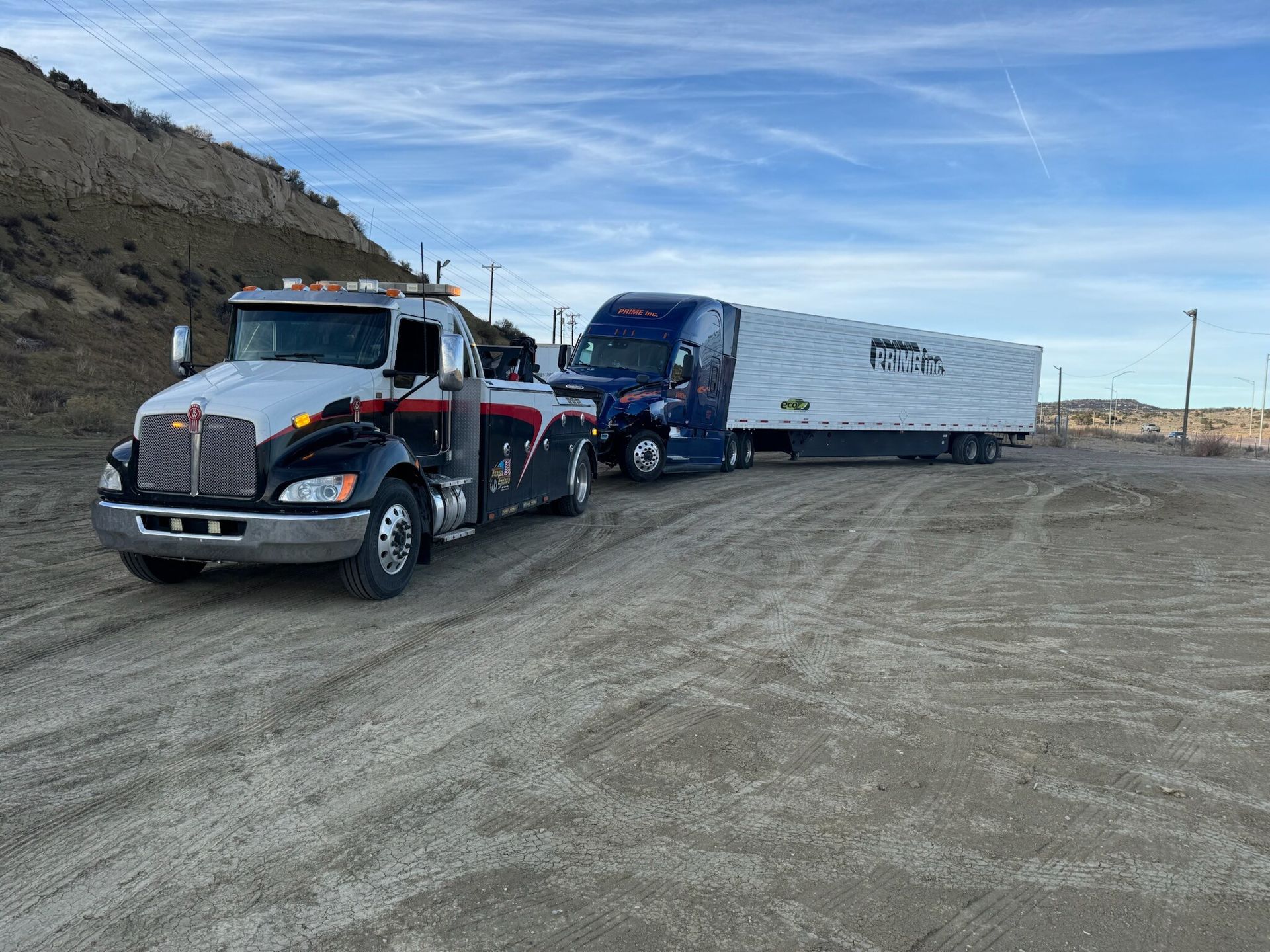 A tow truck is towing a semi truck on a dirt road.