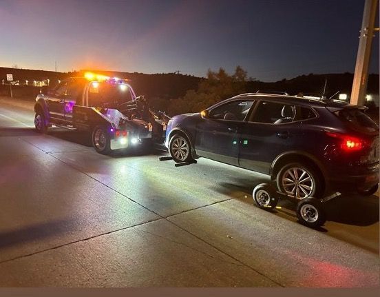 A car is being towed by a tow truck on a highway at night.