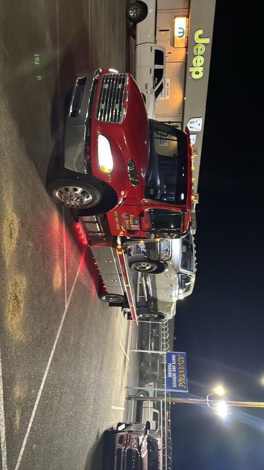 A red jeep is being towed by a tow truck in a parking lot.