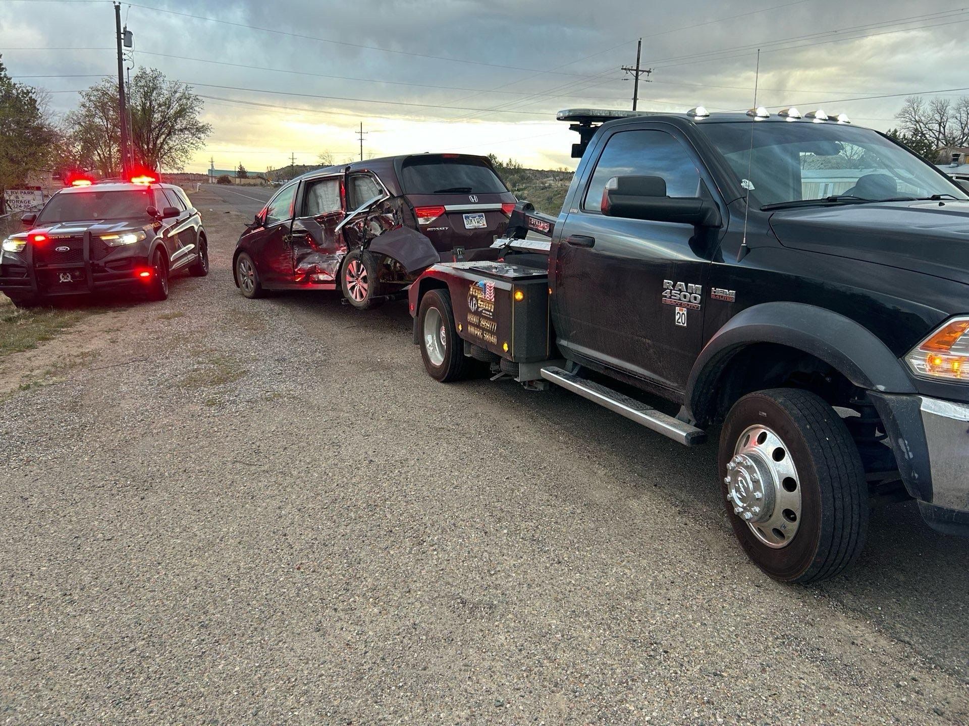 A tow truck is towing two cars on a gravel road.