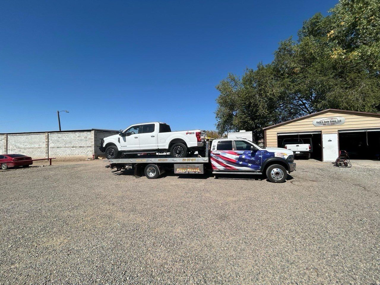 Two trucks are being towed by a tow truck in a gravel lot.