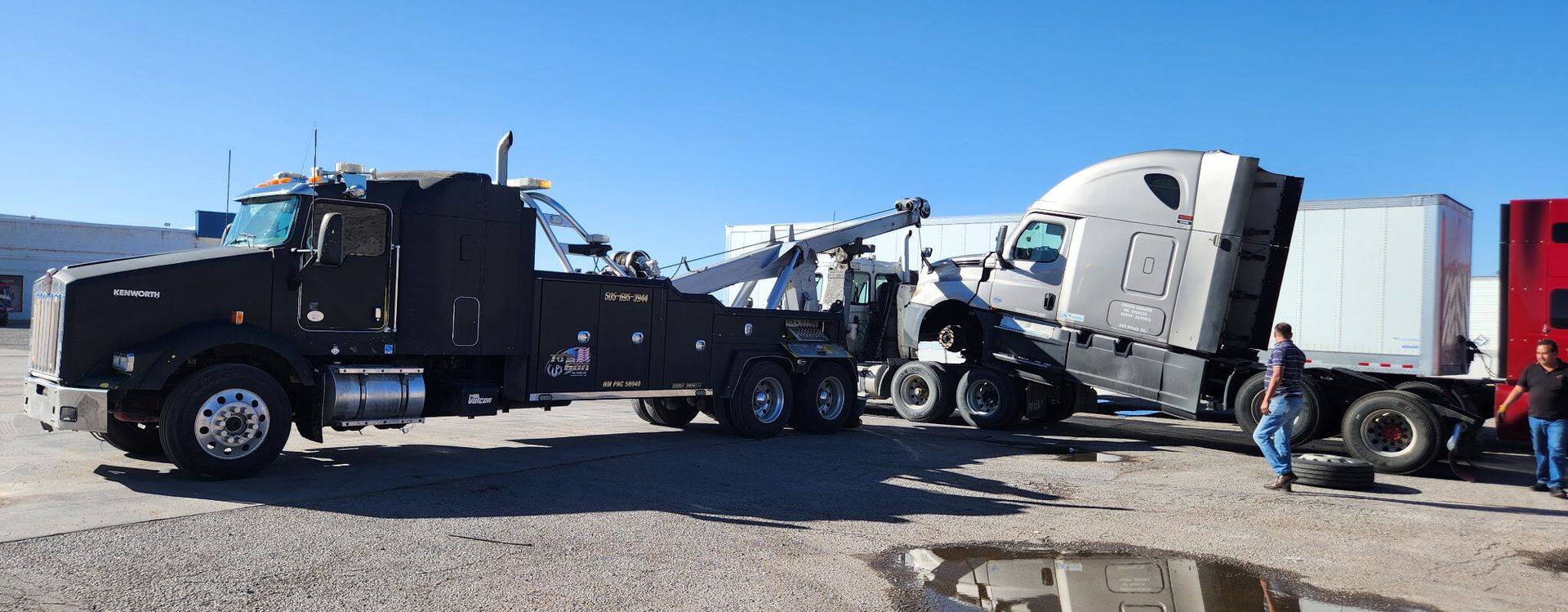 A tow truck is towing a semi truck in a dirt field.