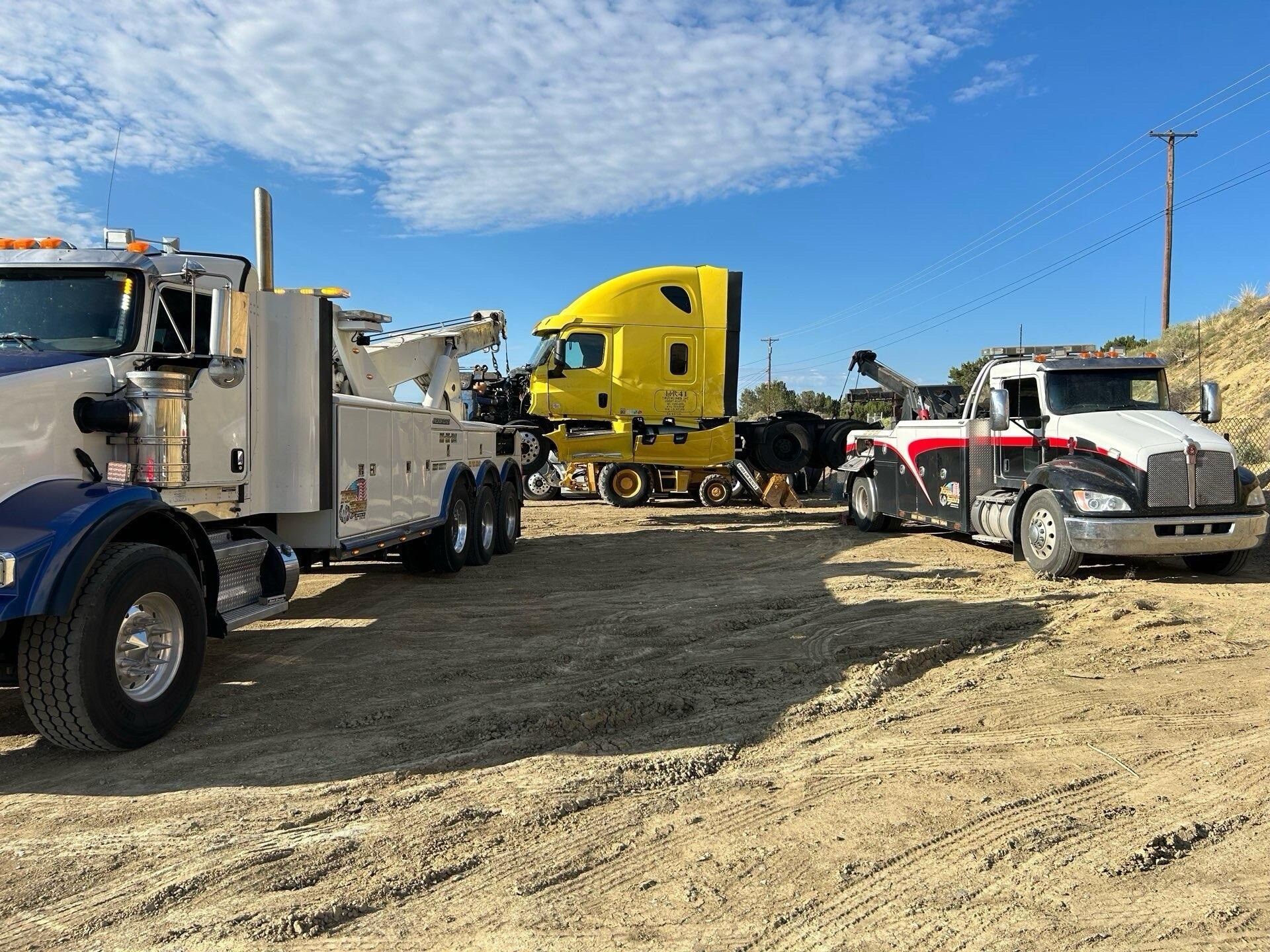 A yellow semi truck is being towed by a tow truck in a dirt field.