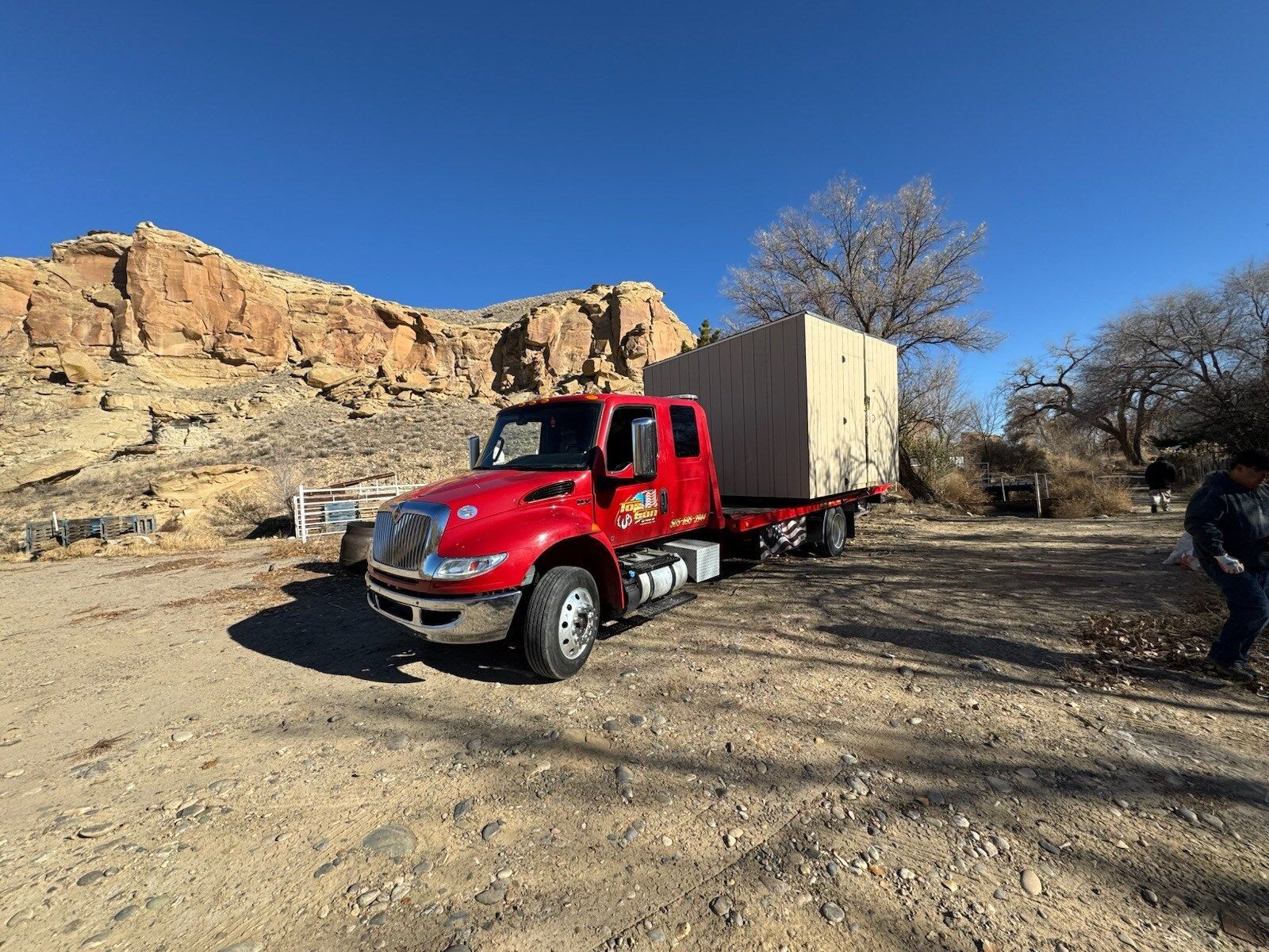 A red truck with a trailer is parked in a dirt field.