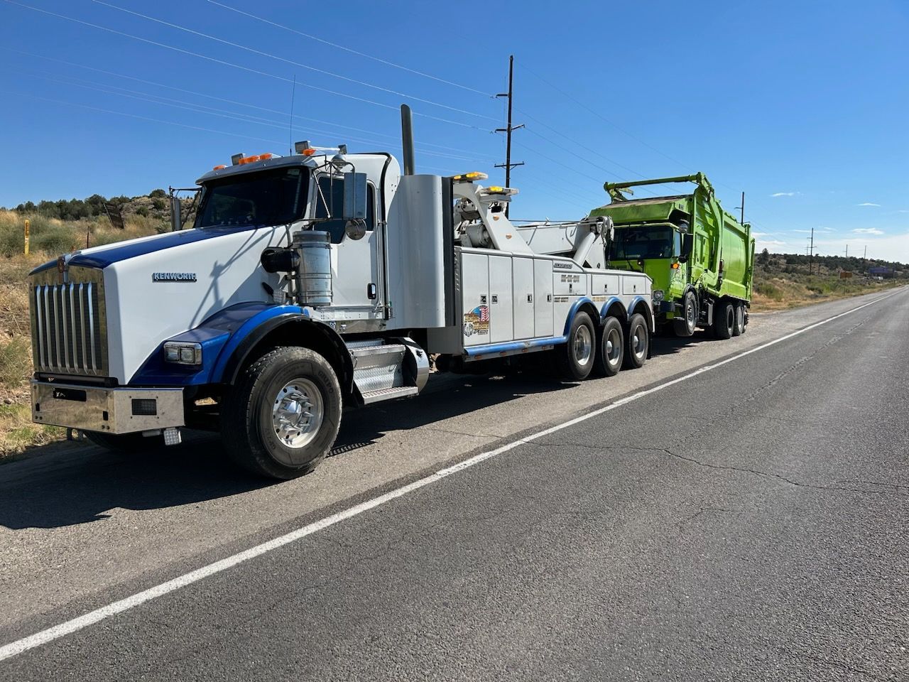 A tow truck is driving down the road next to a dump truck.