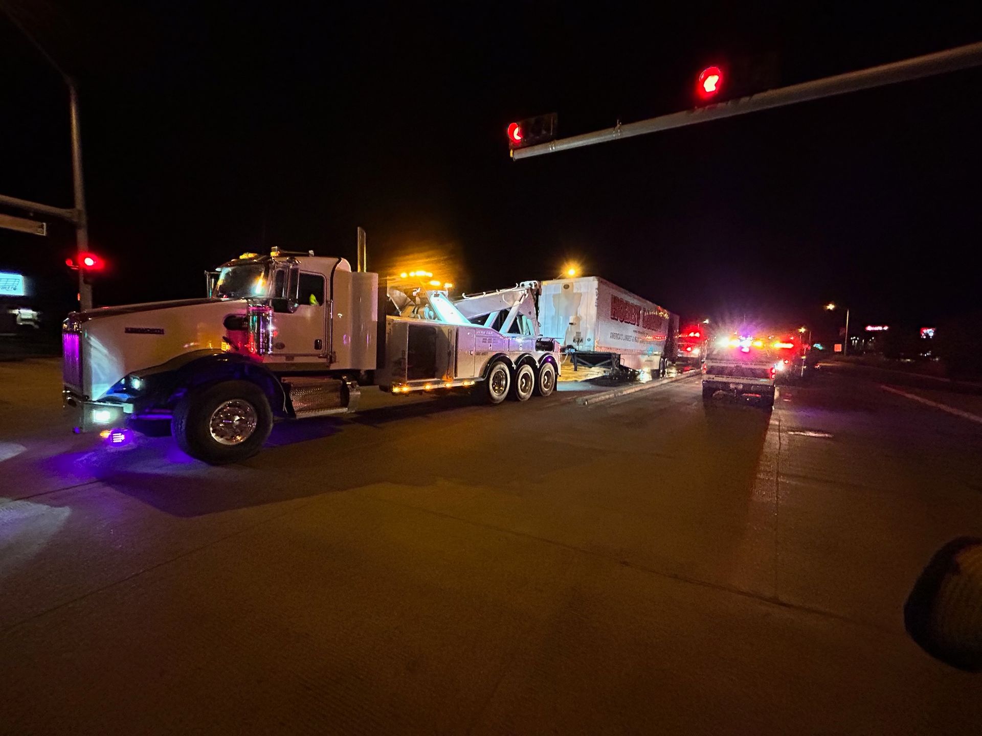 A tow truck is towing a trailer down a highway at night.