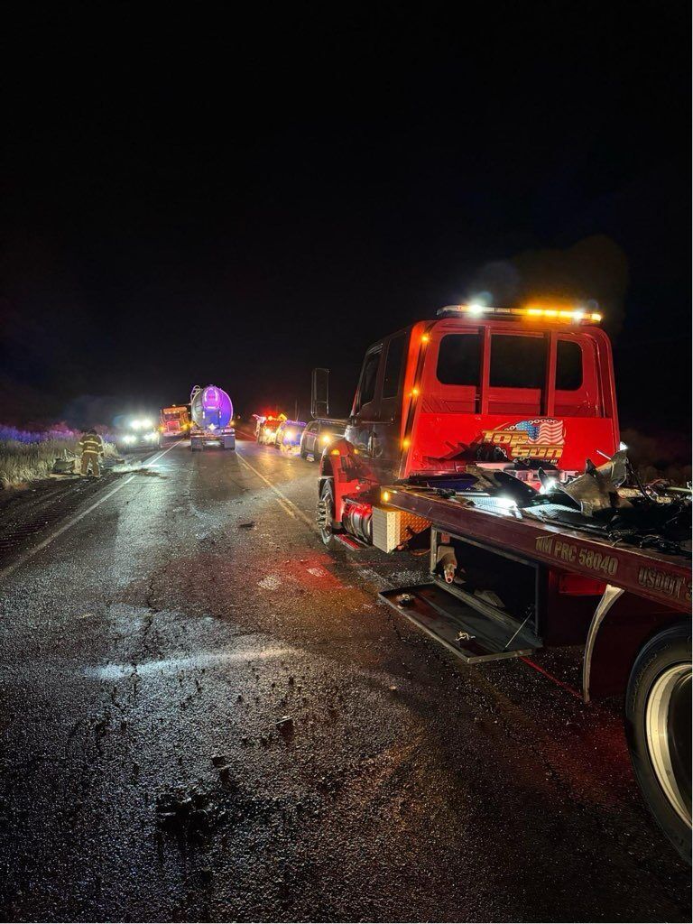 A tow truck is sitting on the side of a highway at night.