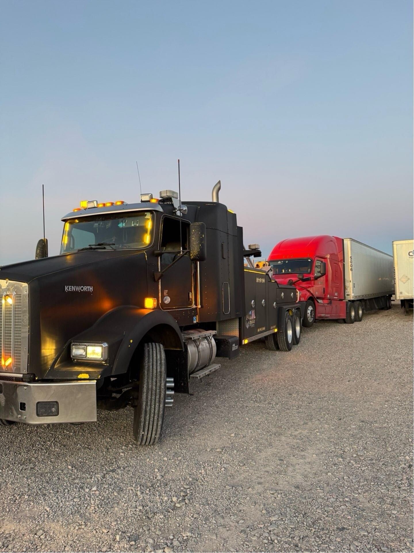 A row of semi trucks are parked in a gravel lot.