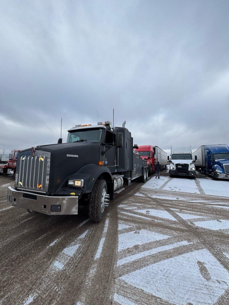 A row of semi trucks are parked in a snowy lot.