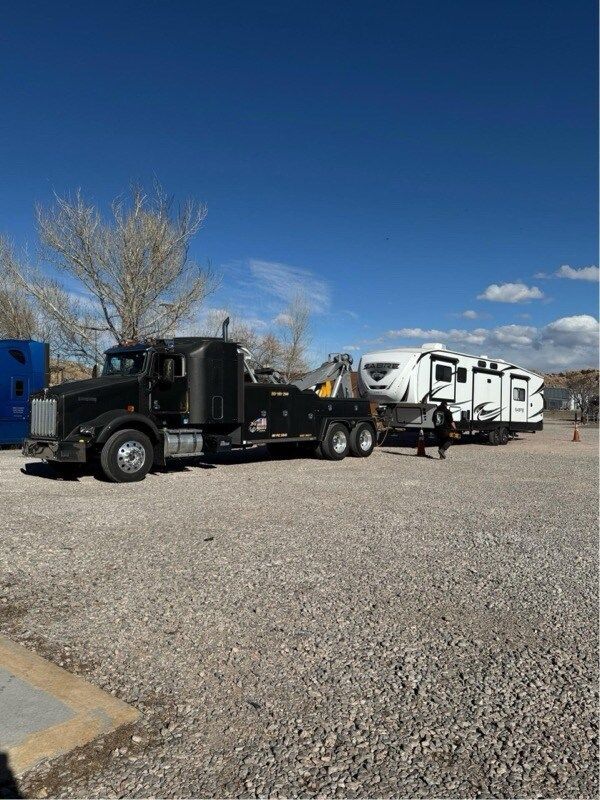 A tow truck is towing a trailer in a gravel lot.