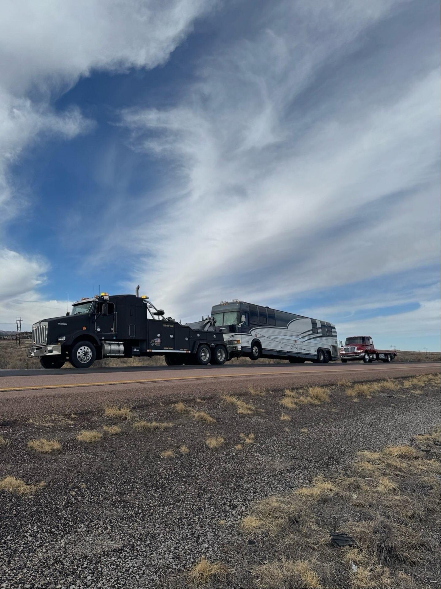 A tow truck is towing a rv down a dirt road.