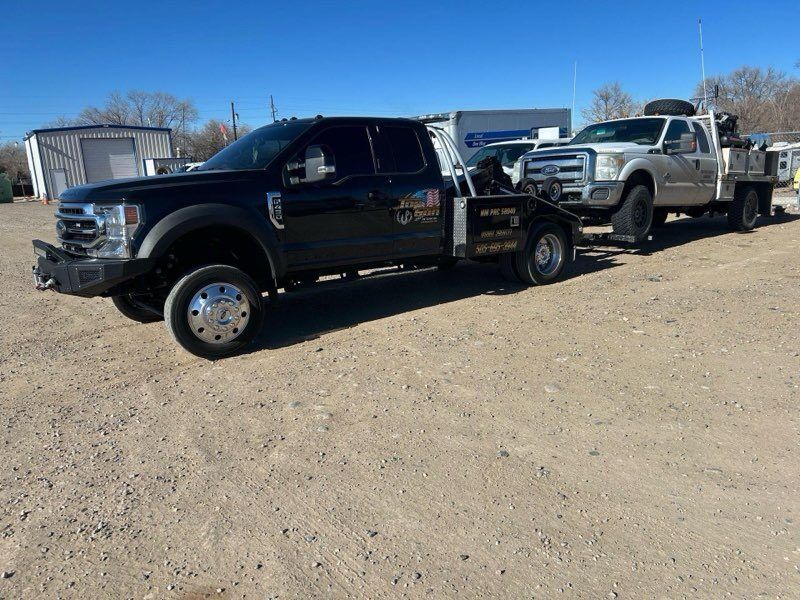 Two tow trucks are parked next to each other in a dirt lot.