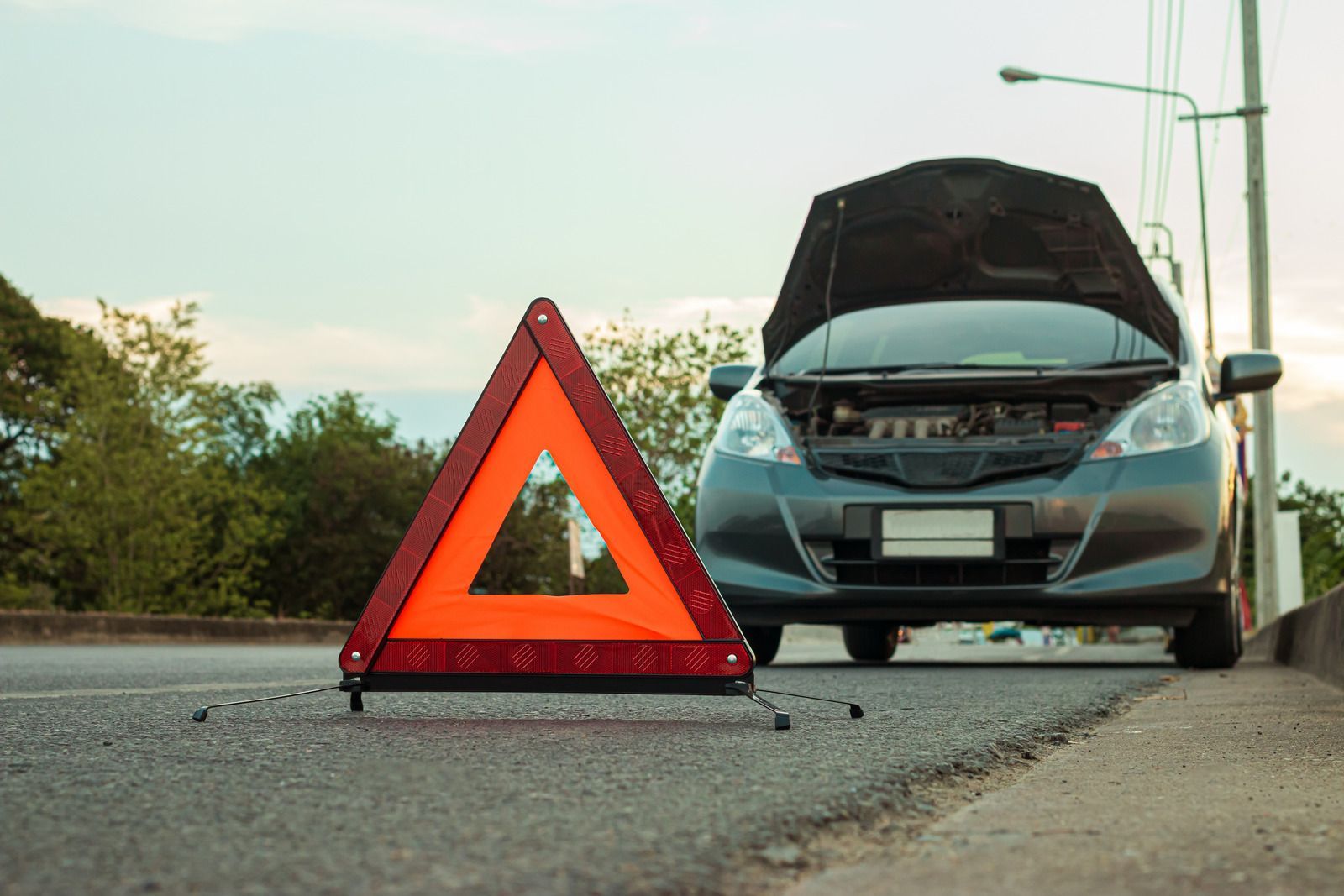 A car with the hood up and a warning triangle on the side of the road.