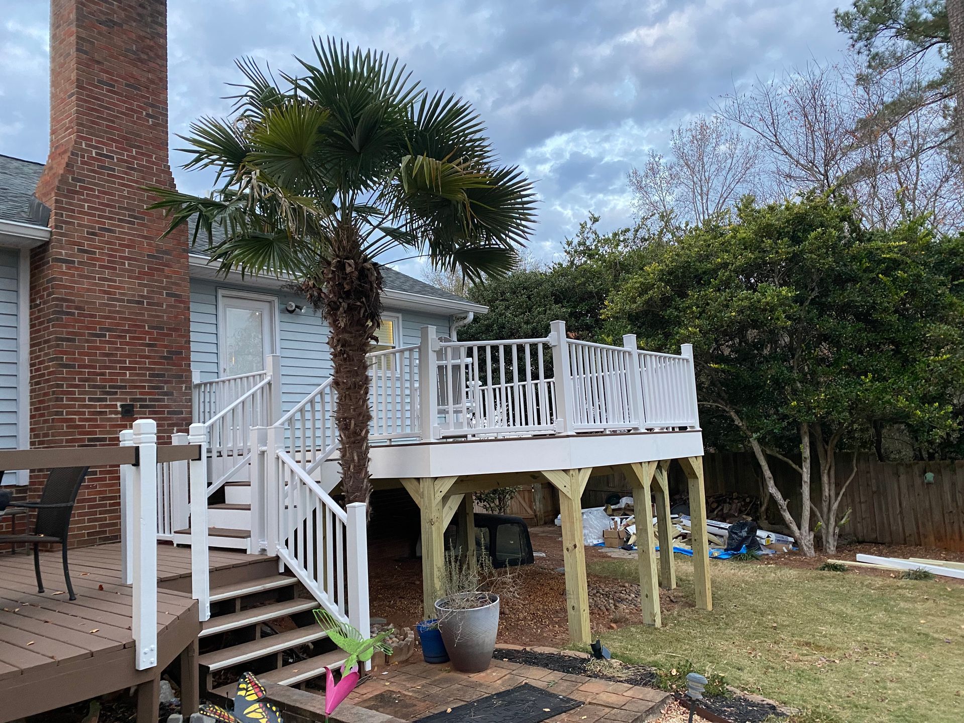 A white deck with stairs and a palm tree in the backyard of a house.