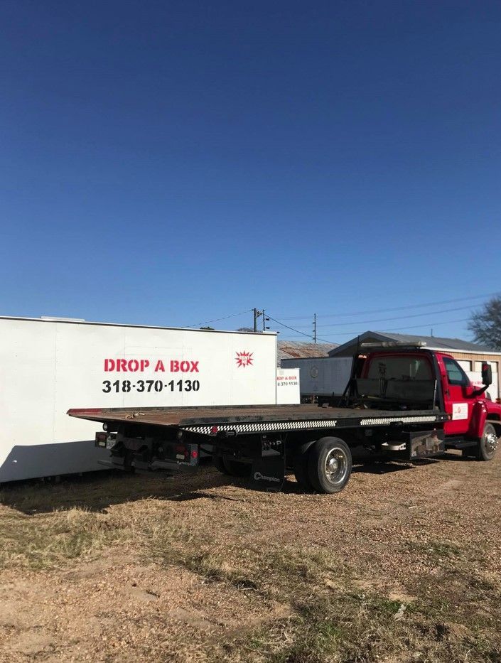 A red tow truck is parked in a field next to a white box.