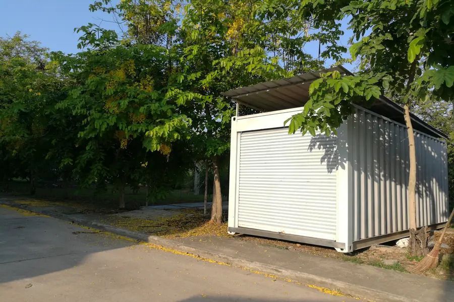 A small white building with a roof is sitting on the side of the road next to trees.