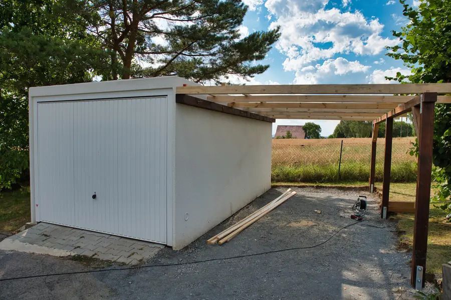 A white garage with a wooden pergola attached to it.