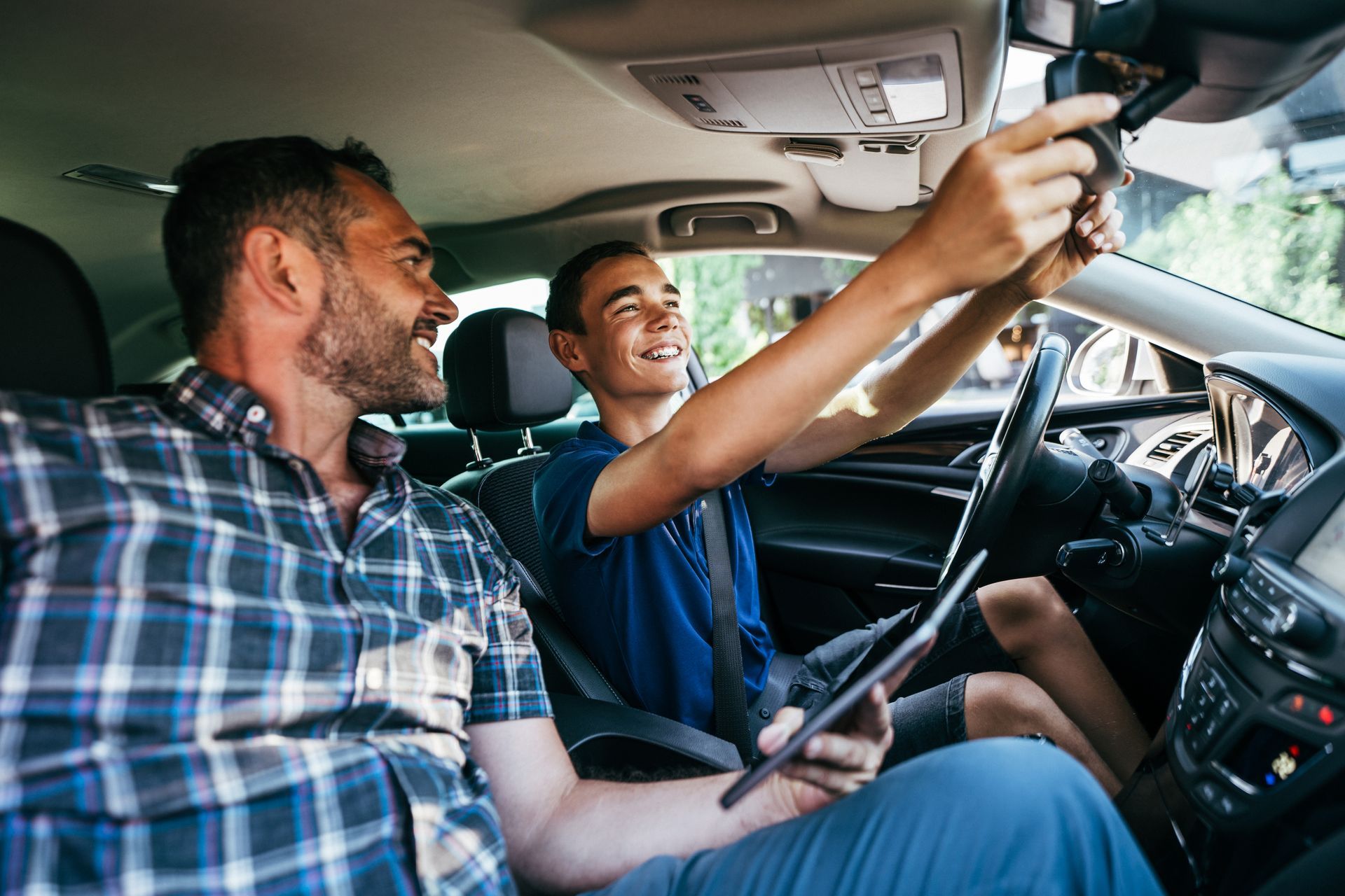 A driving instructor and his student in a car cabin explaining how to prepare the safety mirror.