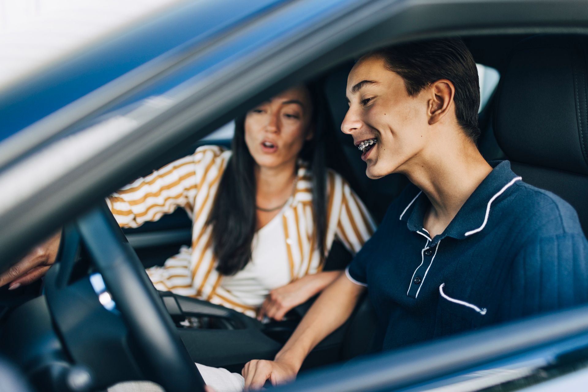 Happy teenage boy getting driving lessons from mother while sitting in car Happy teenage boy getting driving lessons from mother while sitting in car