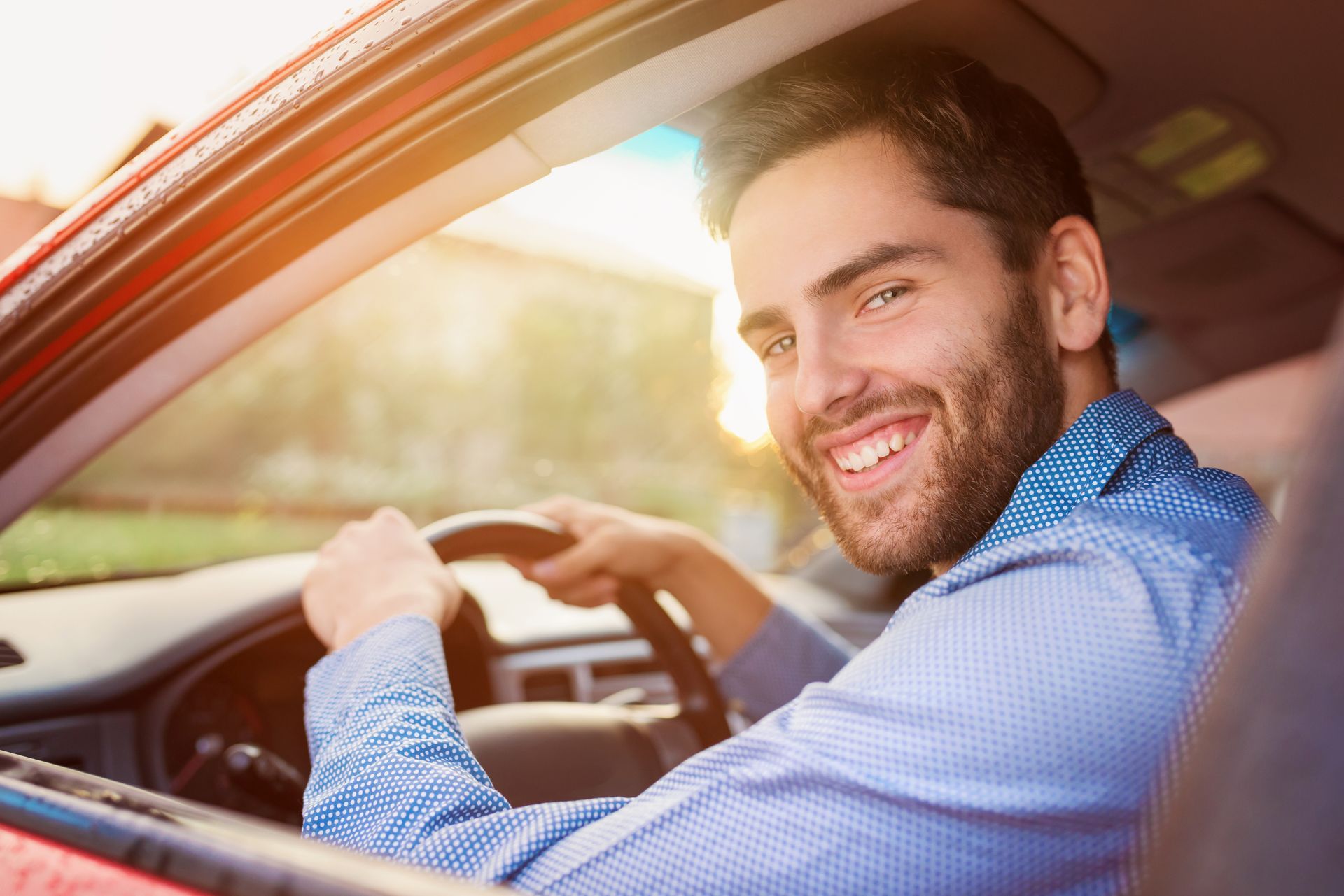 Man smiling while driving a car, with sunlight shining through the window.