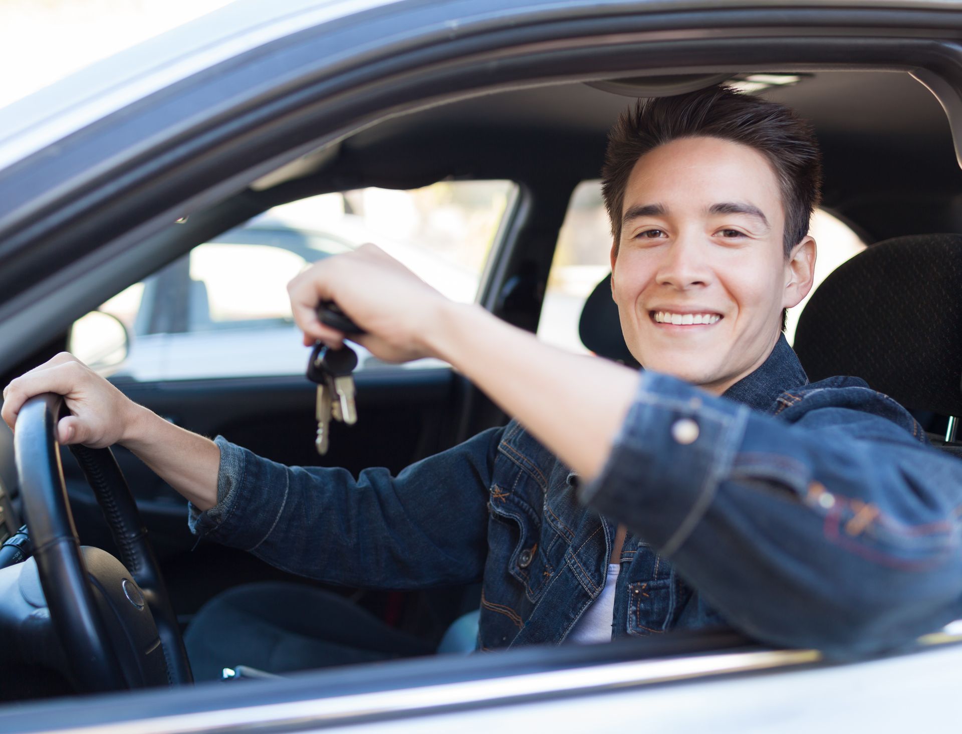 Young man in car, smiling and holding car keys.