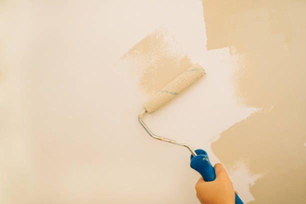 A hand uses a roller to apply paint to a wall during a home painting job.