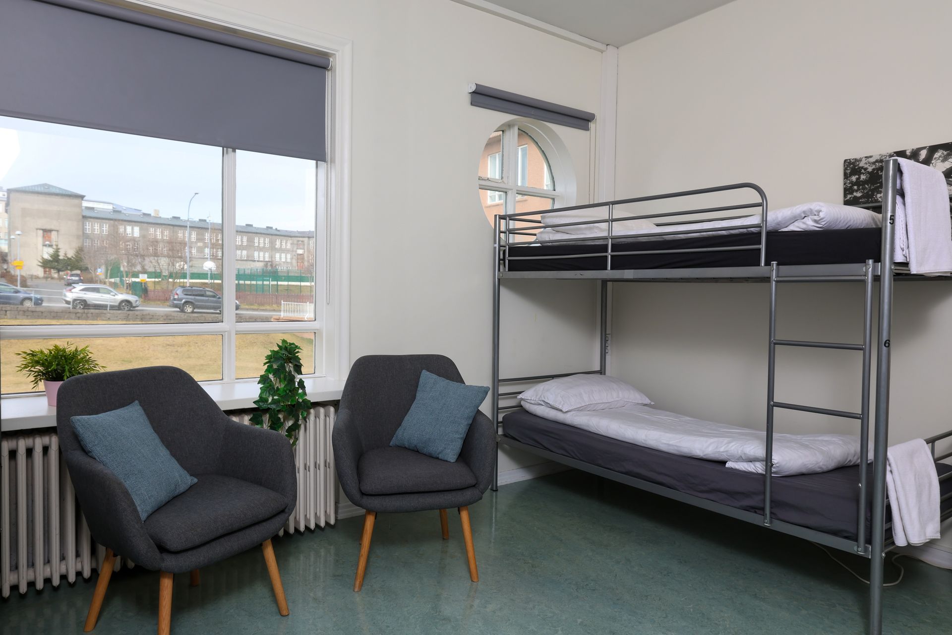 A bunk bed is in a room with two chairs and a window.