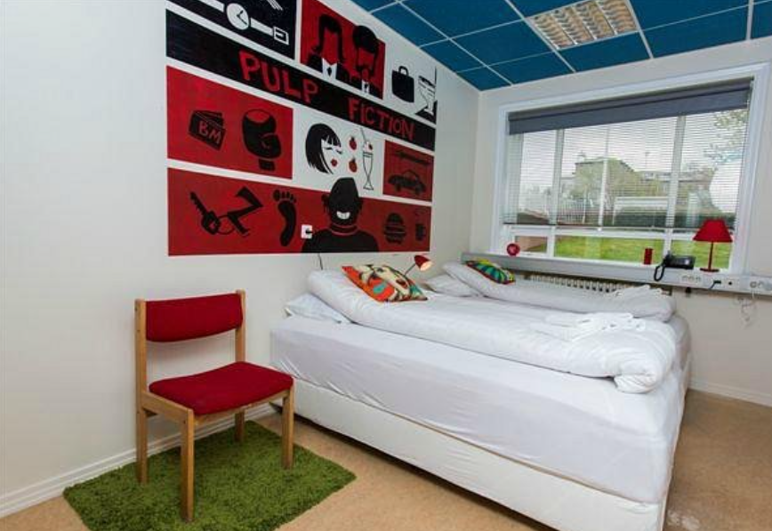 A bedroom with two beds and a chair and a painting on the wall that says pulp fiction