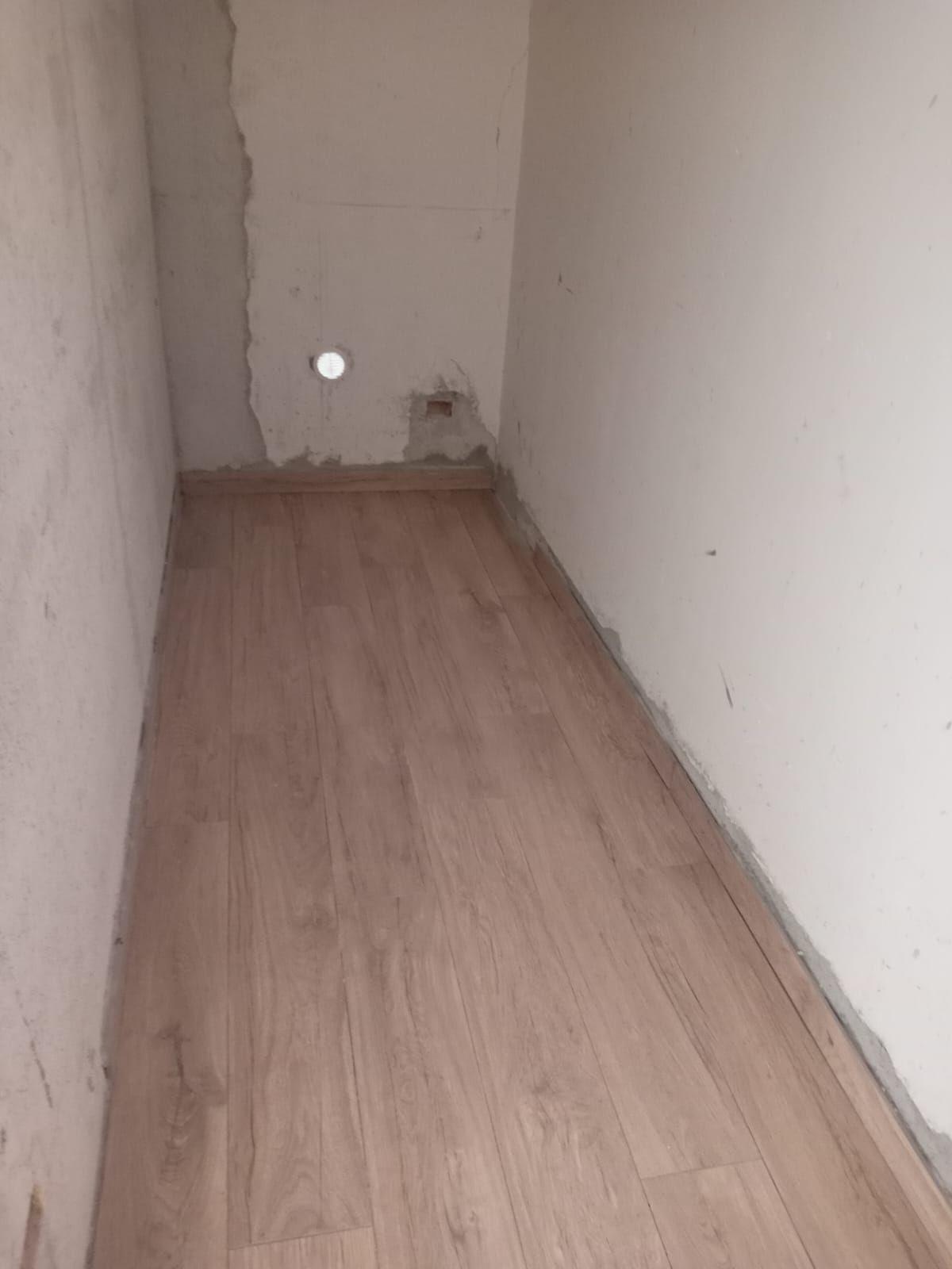 un lungo corridoio con pavimento in legno e pareti bianche .