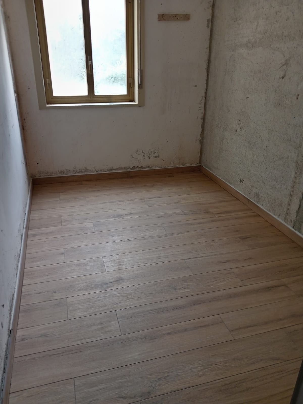 una stanza vuota con un pavimento in legno e una finestra .