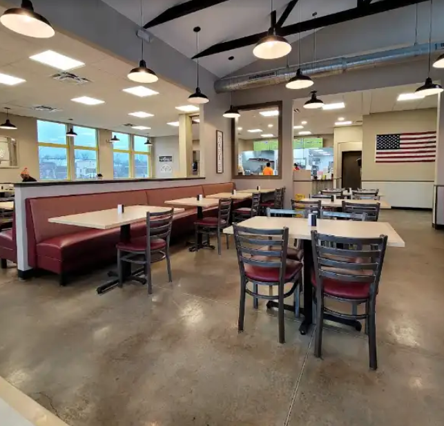 Restaurant interior with booths, tables, and chairs. American flag on wall, pendant lights.