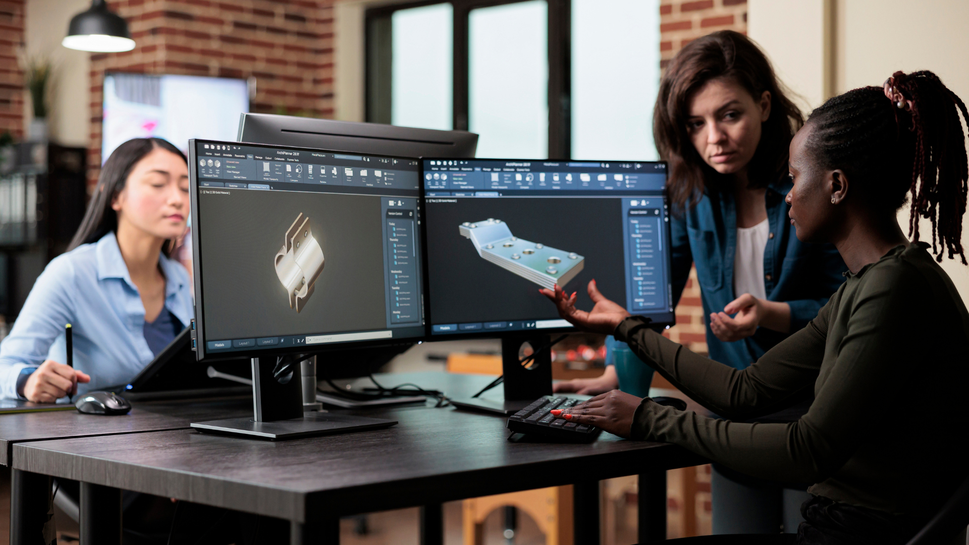 A group of women are sitting at a desk in front of computer monitors.