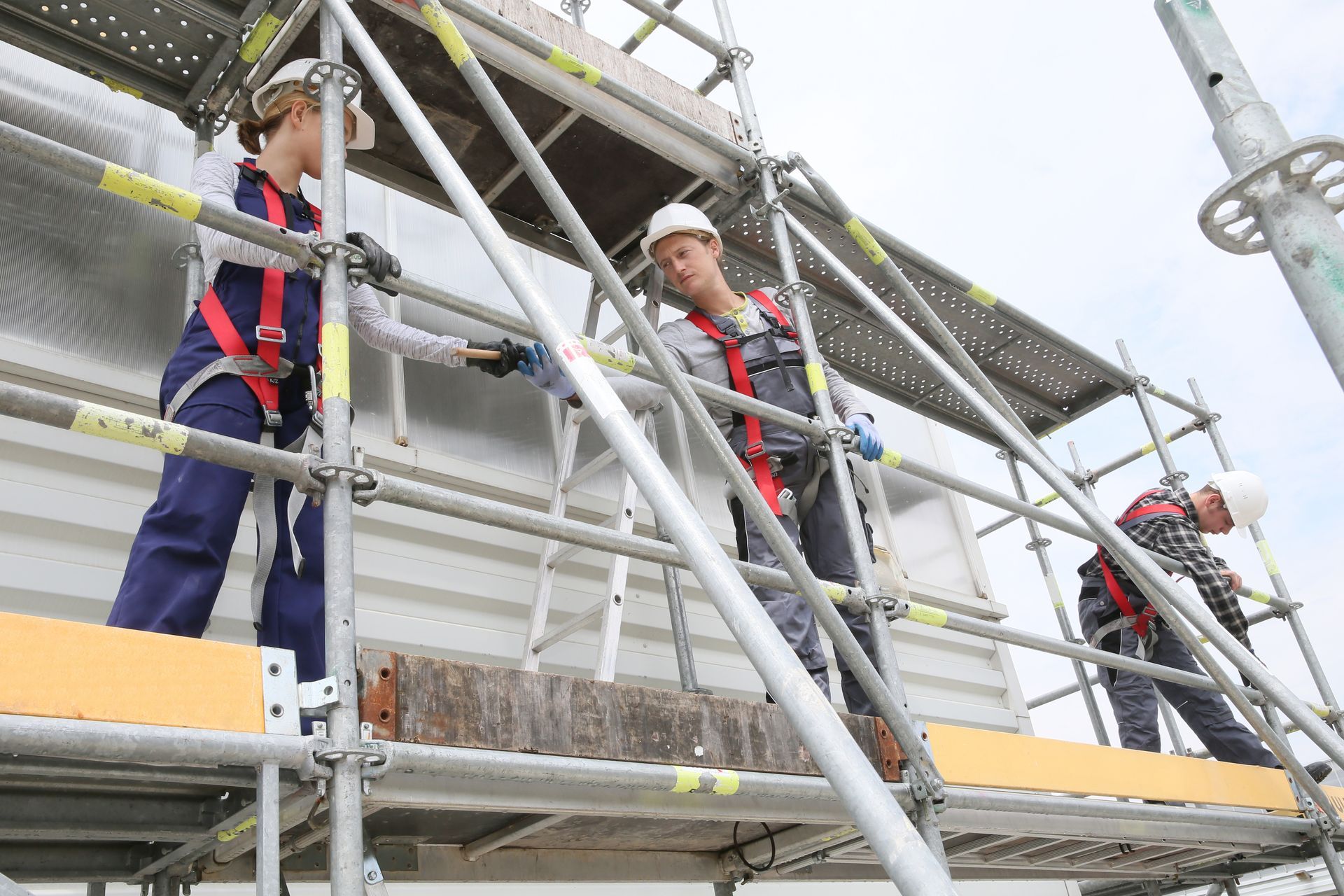 A group of builders wearing protective gear is installing scaffolding on site. A group of builders wearing protective gear is installing scaffolding on site.