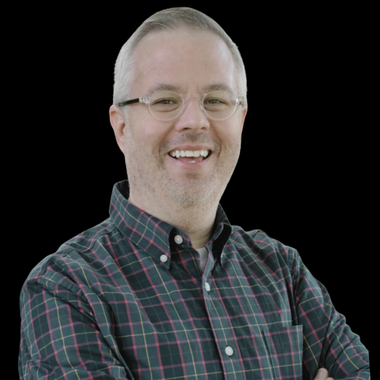 White man with short grey hair and a bow tie against brick wall with University of Minnesota logo painted on it