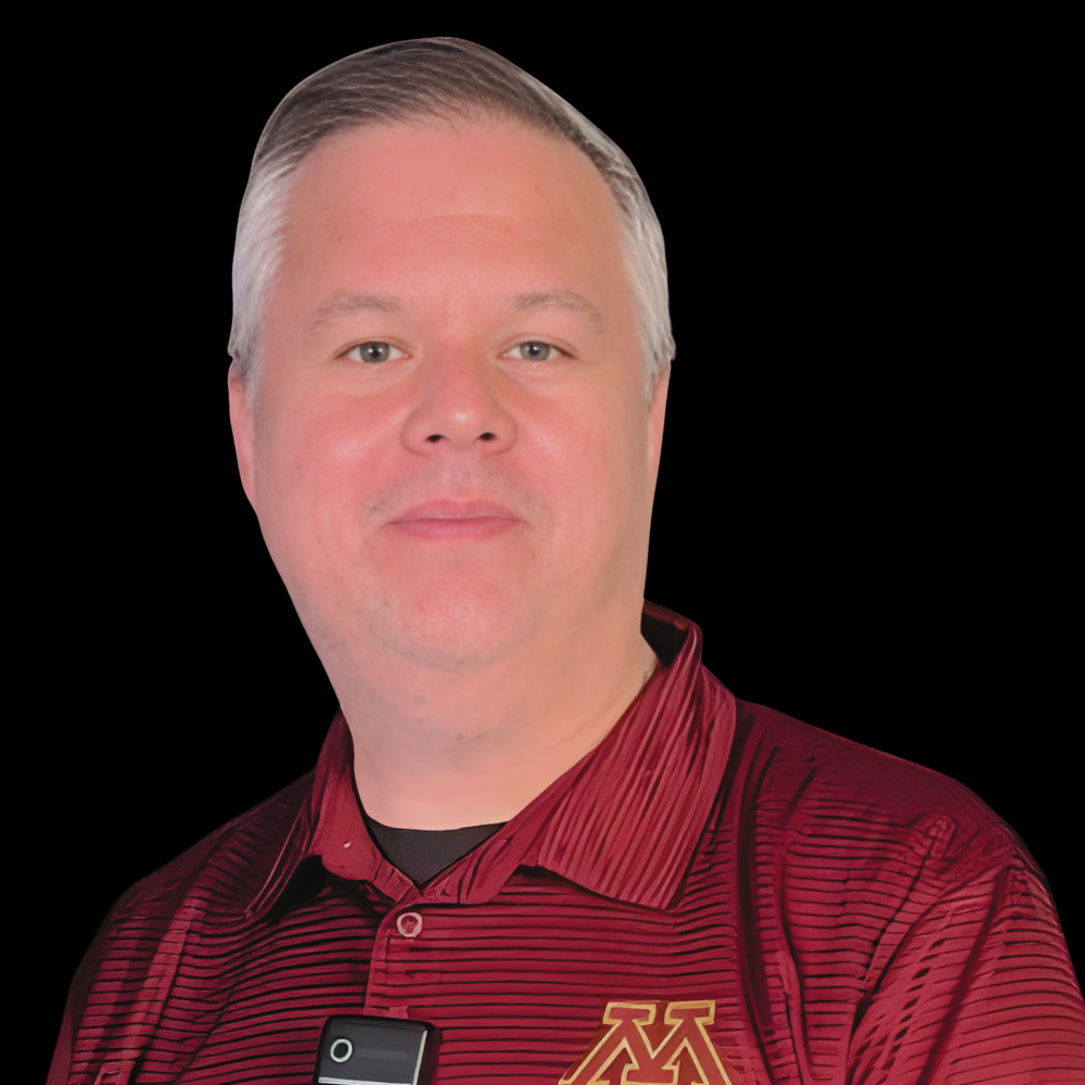 White man with short grey hair and a bow tie against brick wall with University of Minnesota logo painted on it