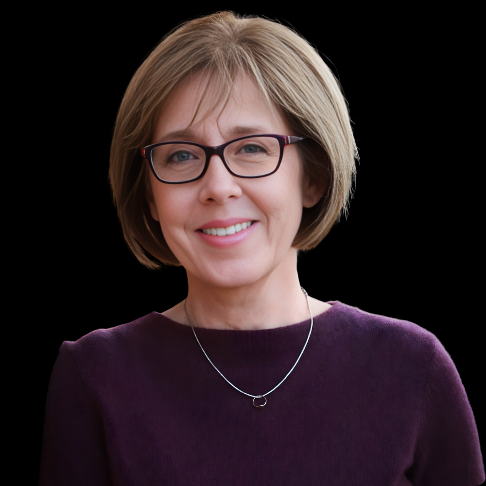 White woman with glasses and short hair smiling against a brick wall