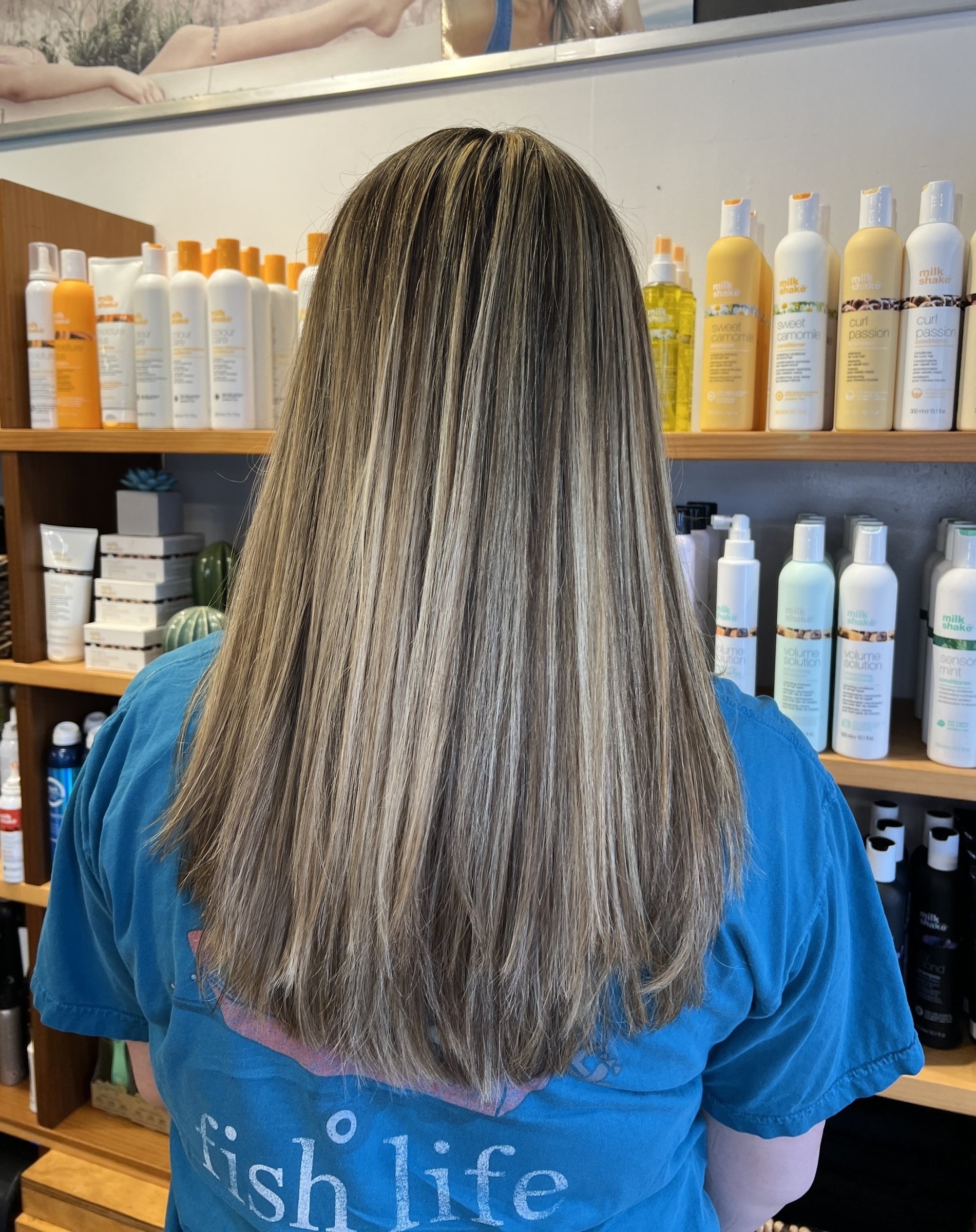 A woman wearing a fish life shirt is standing in front of a shelf of hair products.