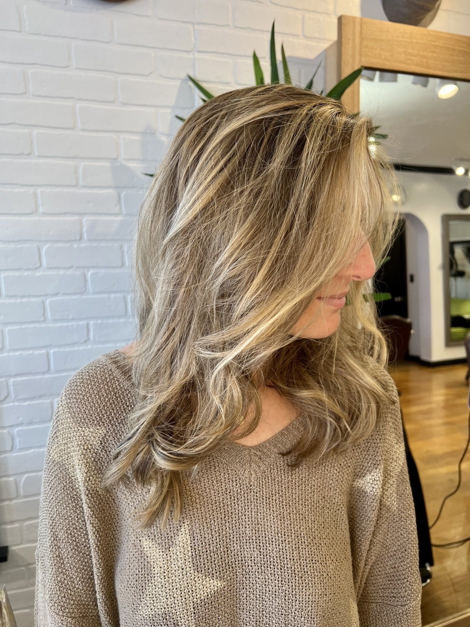 A woman with long blonde hair is wearing a brown sweater.