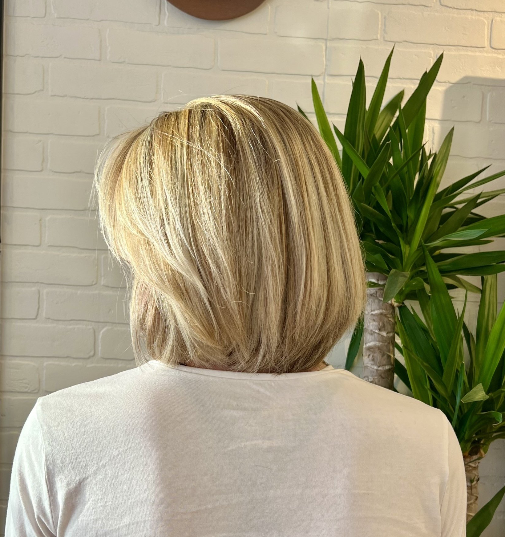 A woman with blonde hair is standing in front of a plant