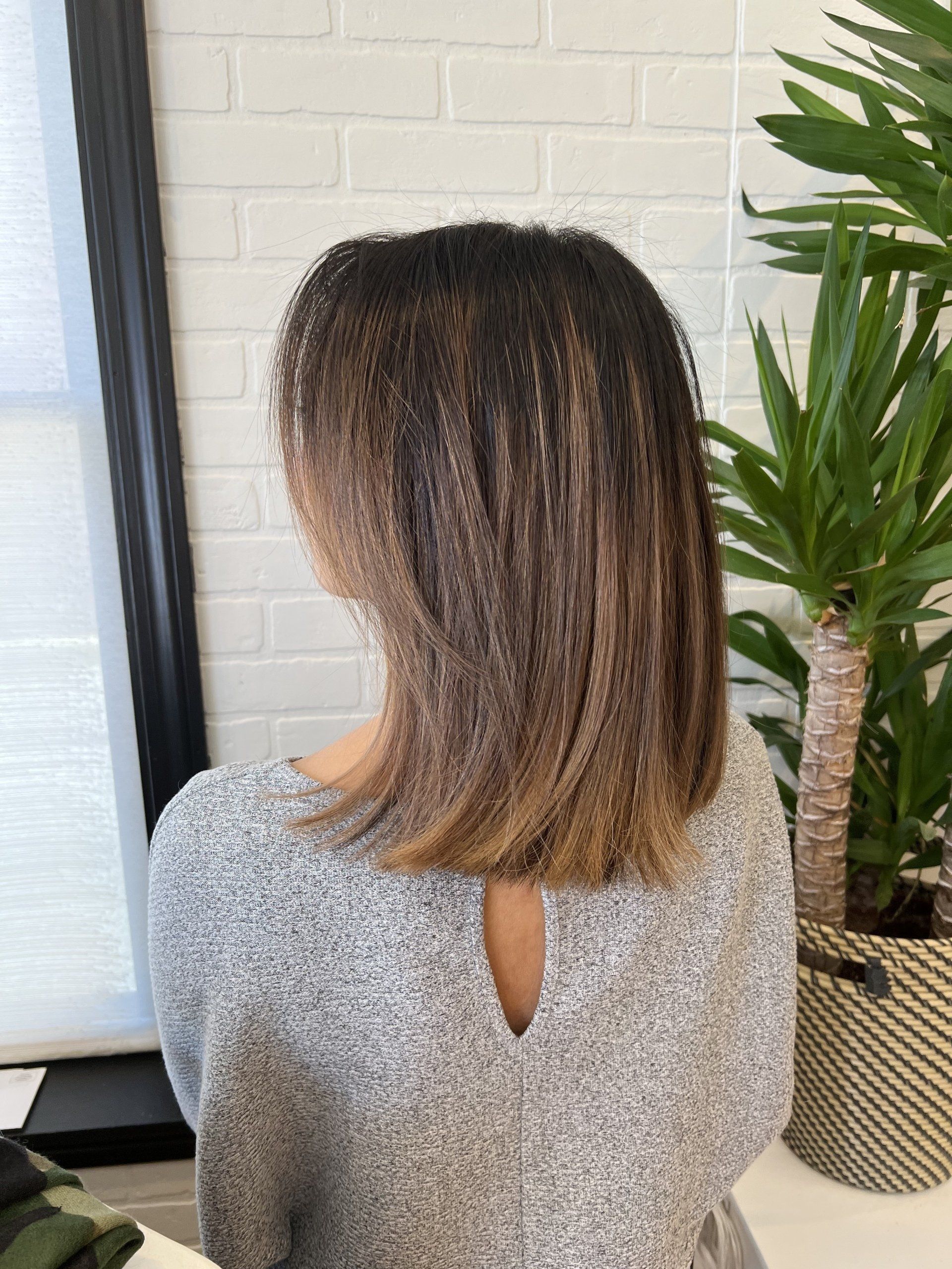 A woman with short hair is sitting in front of a potted plant.