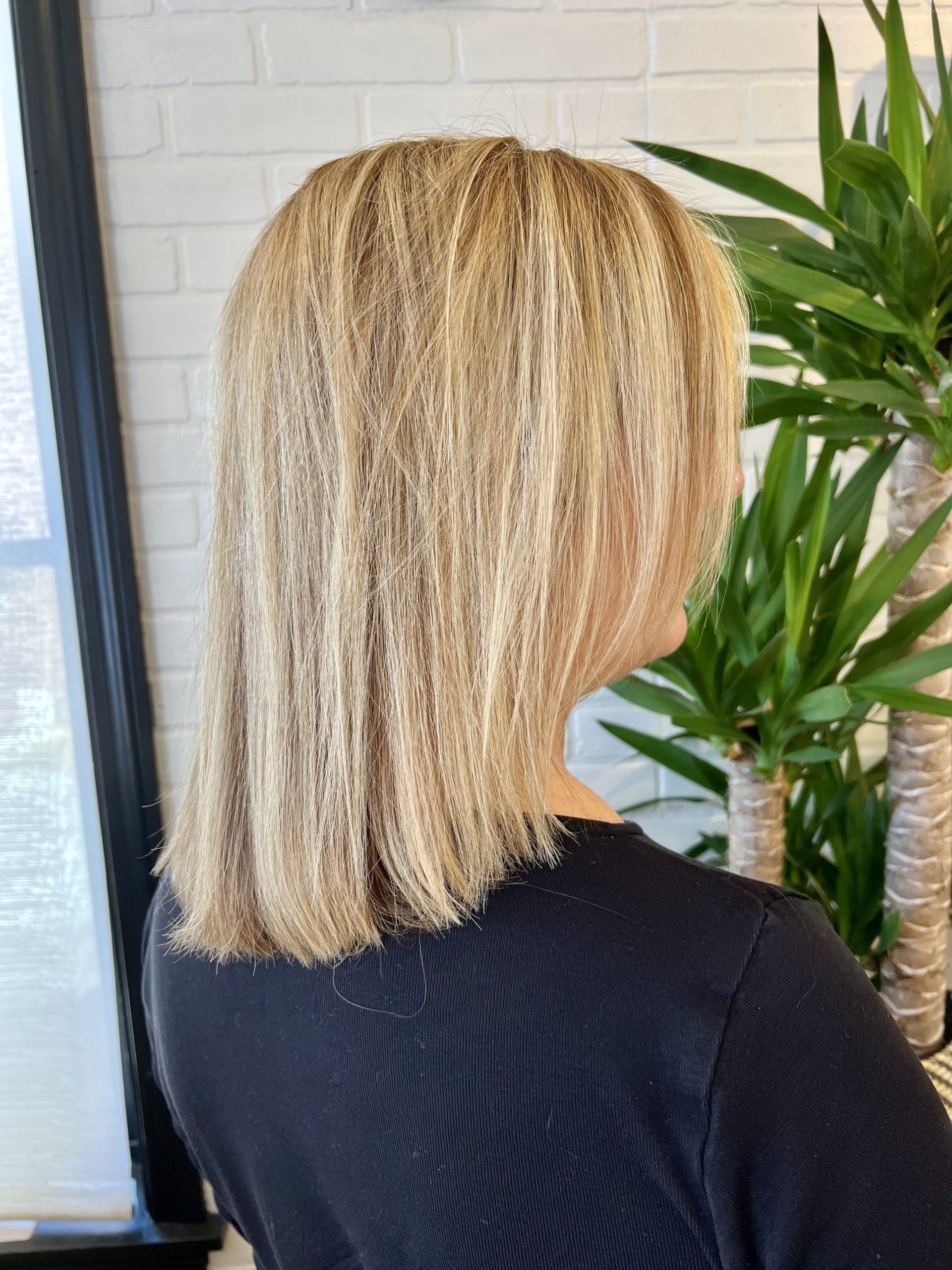 A woman with blonde hair is wearing a black shirt and standing in front of a plant.