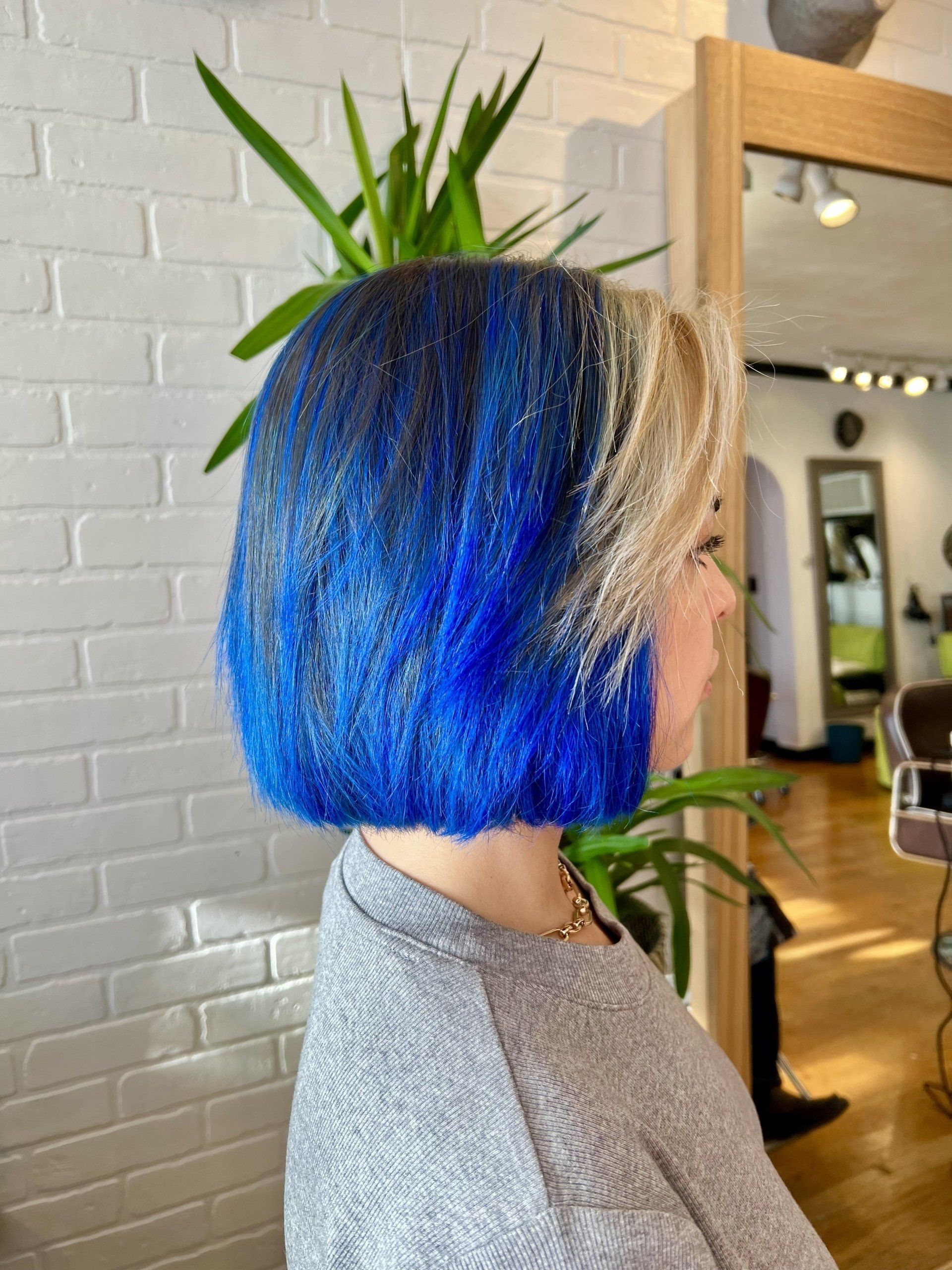 A woman with blue hair is sitting in front of a mirror in a salon.