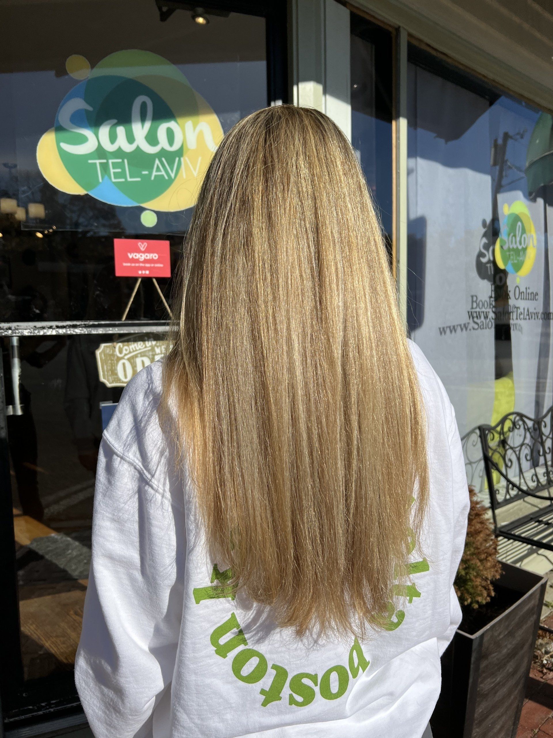 A woman with long blonde hair is standing in front of a salon