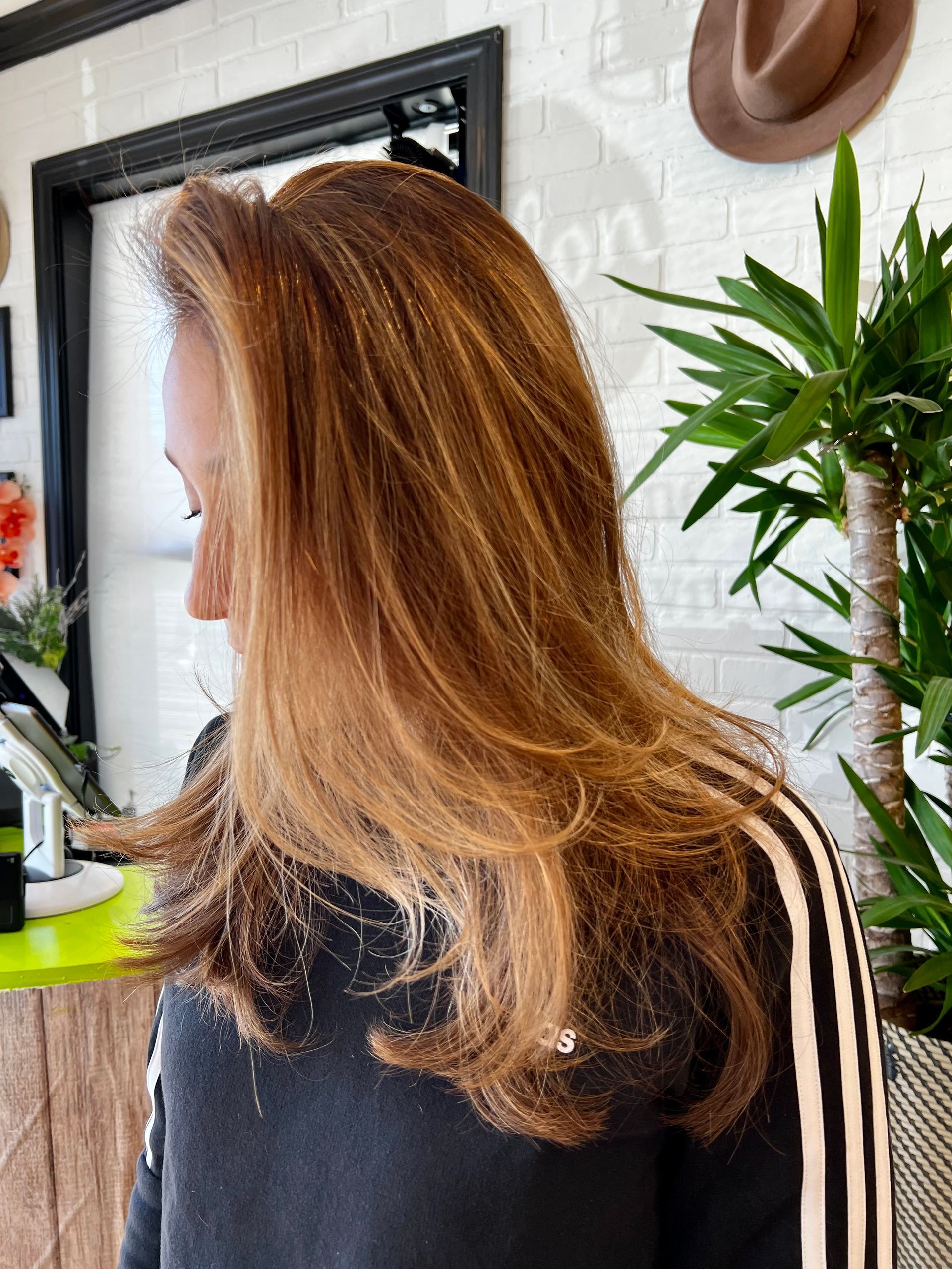 A woman with long brown hair is standing in front of a plant.