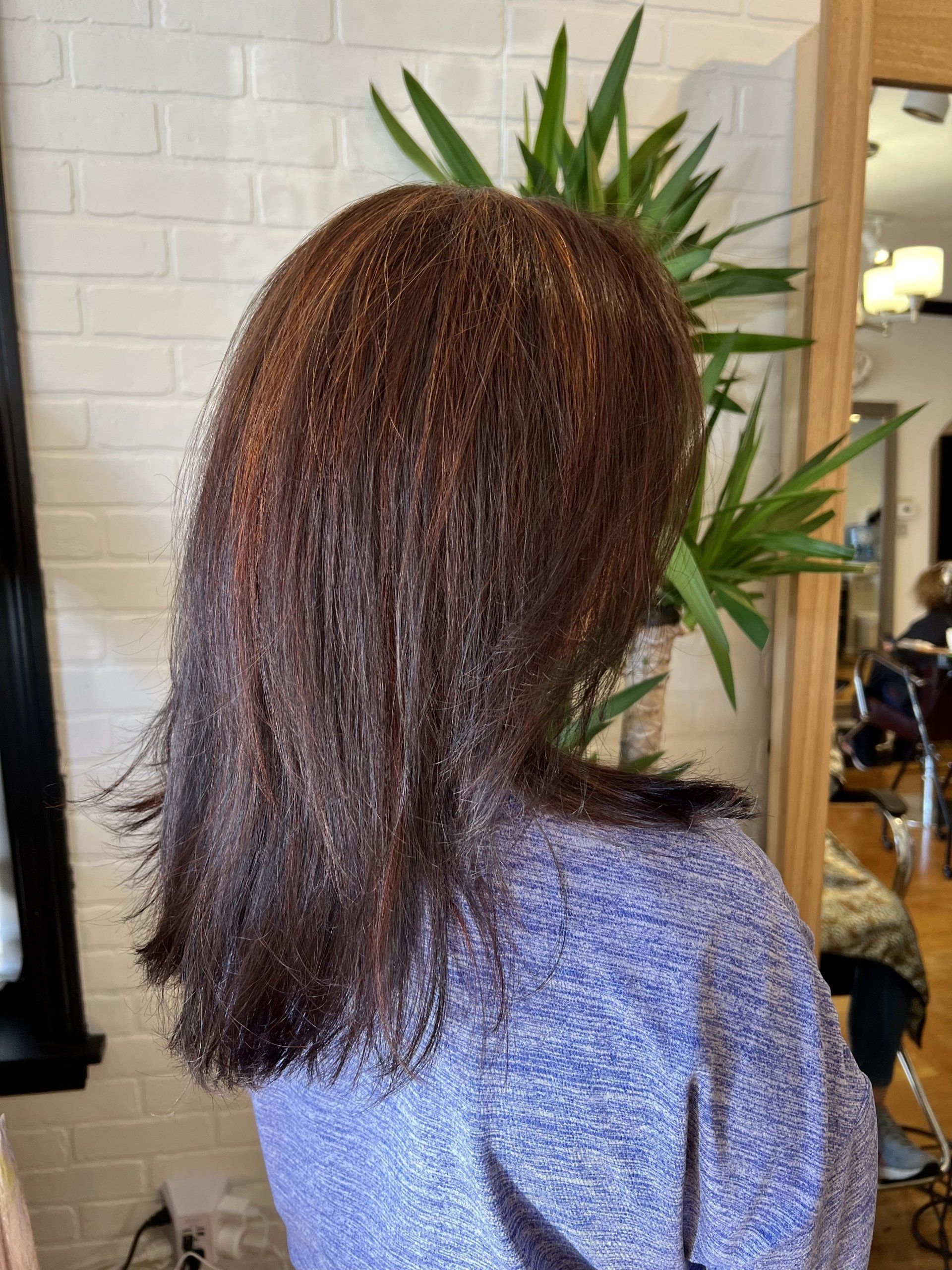 A woman with long brown hair is standing in front of a mirror in a salon.