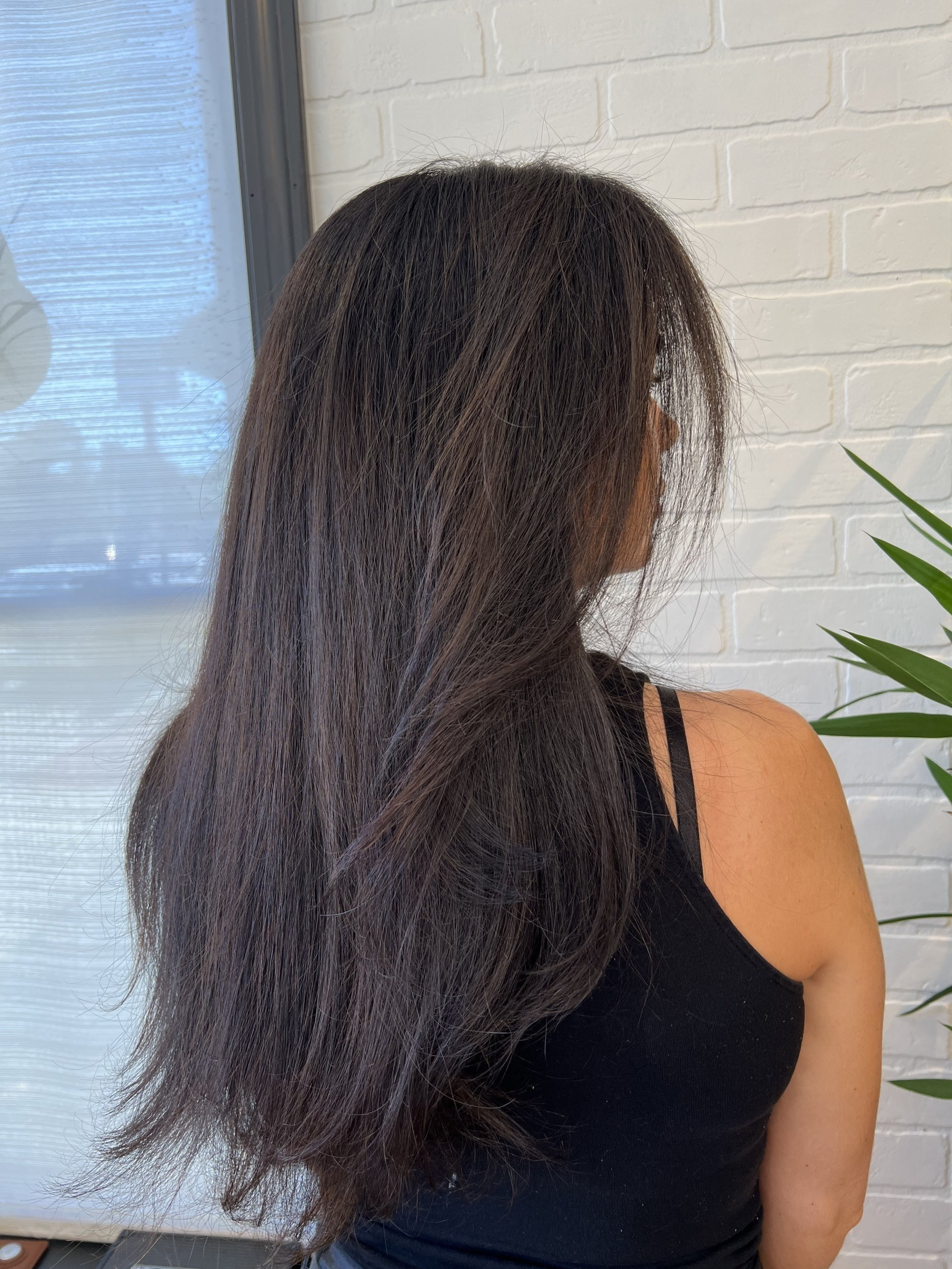 A woman with long hair is standing in front of a white brick wall.