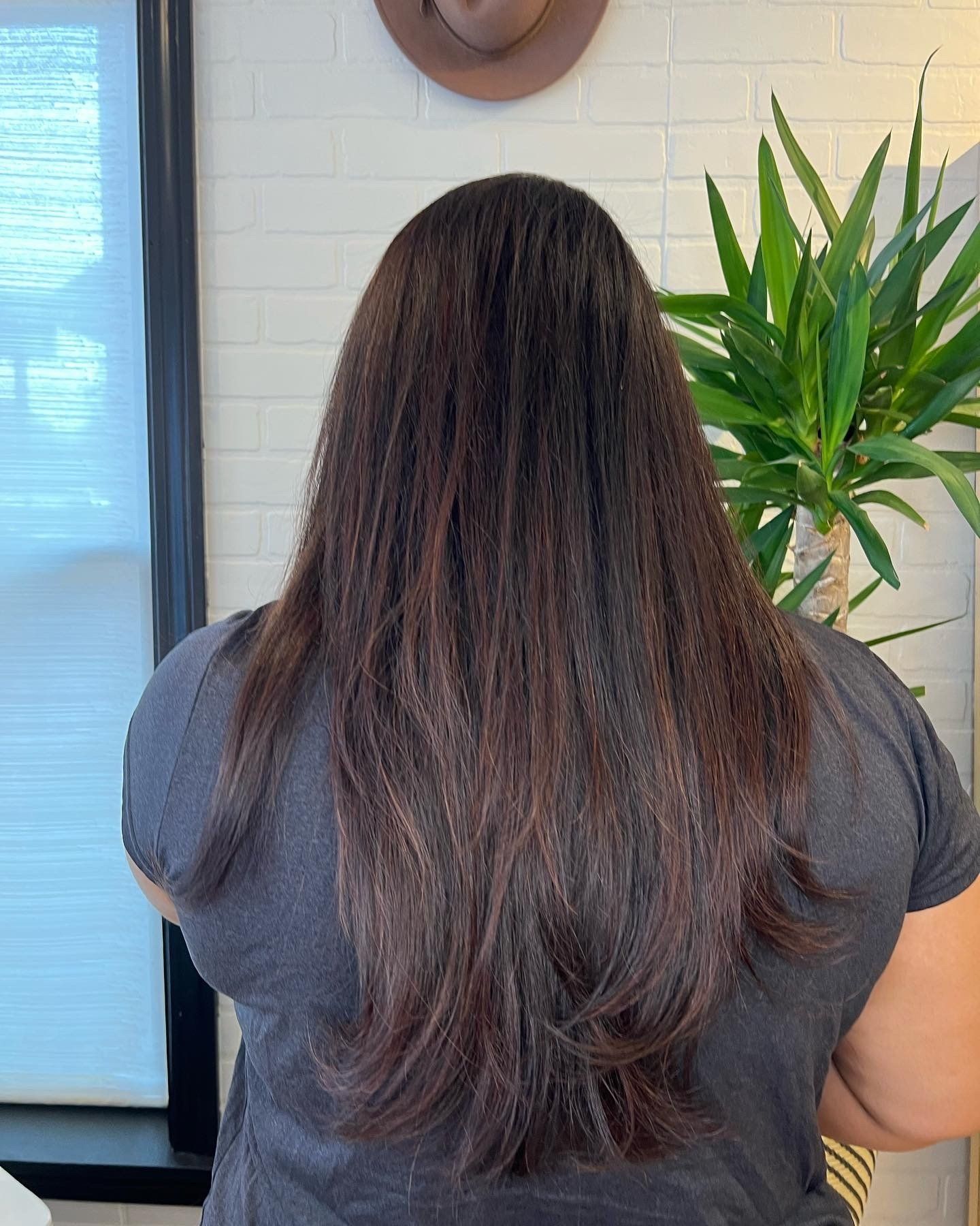 A woman with long brown hair is standing in front of a plant.