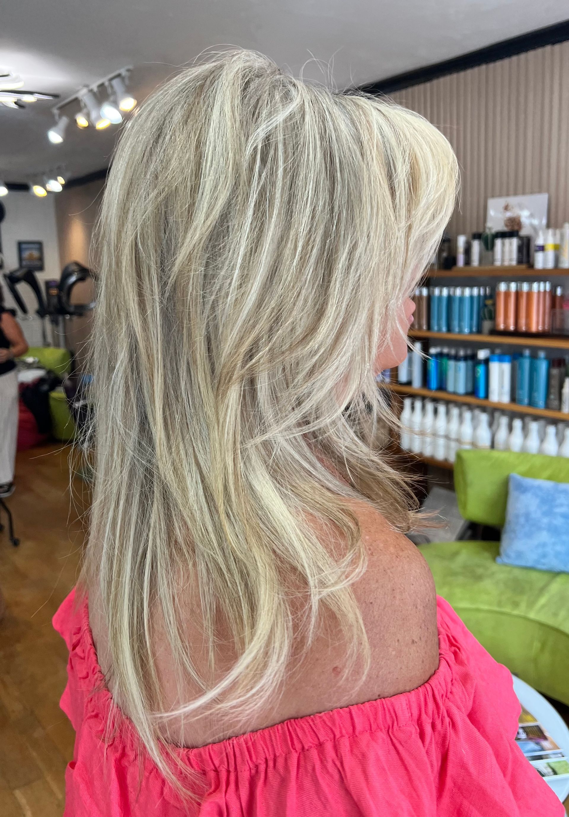 The woman is wearing a pink off the shoulder top and has blonde hair.