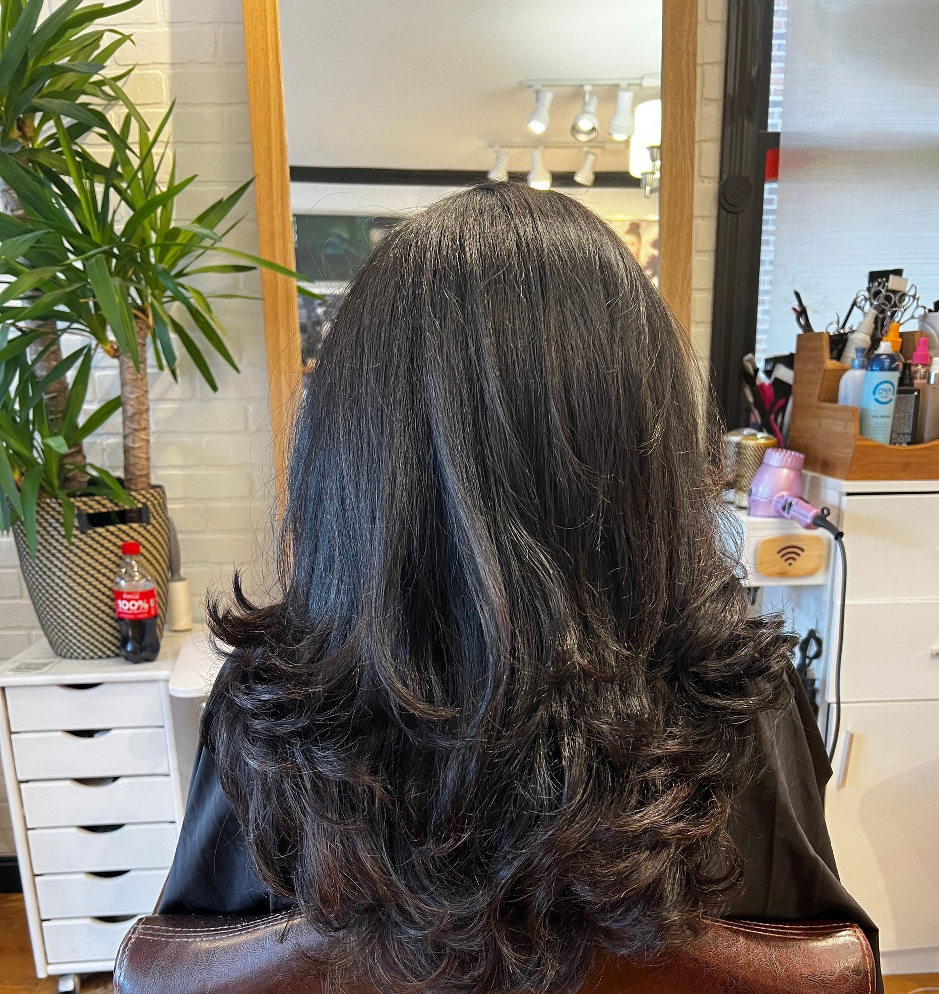 A woman with long hair is sitting in a chair in front of a mirror.